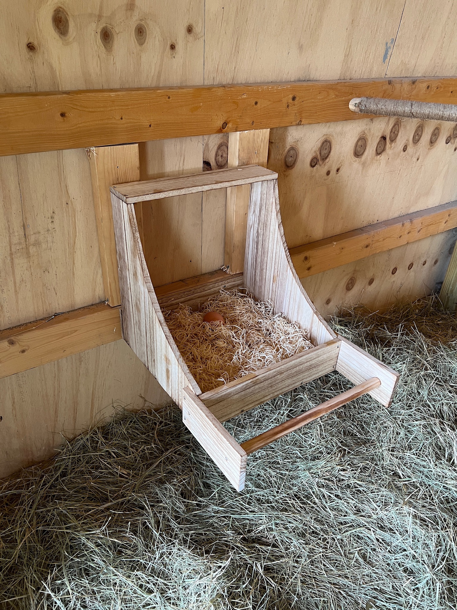 wood nesting box in chicken coop with bedding and egg.
